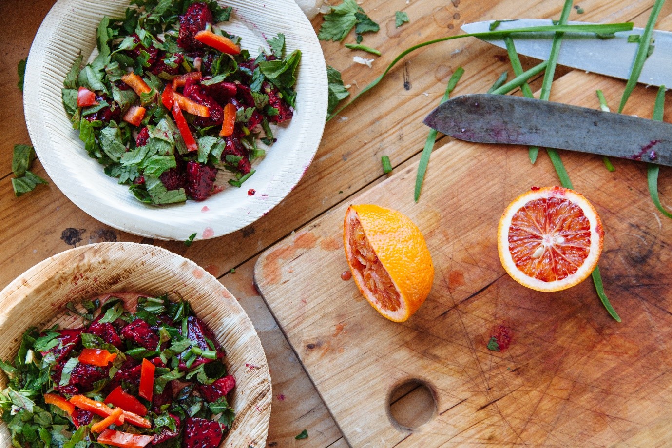 Flat lay of blood orange on chopping board next to bowls of salad