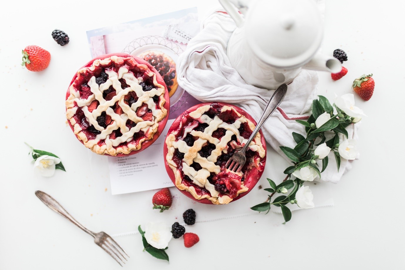 Flat lay of fruit tarts surrounded by strawberries and flowers