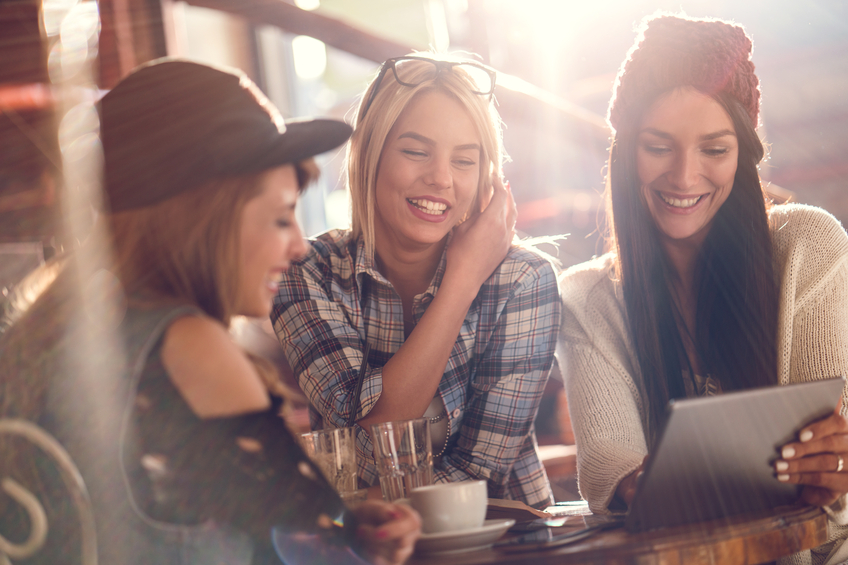 Happy female friends using digital tablet in a cafe.