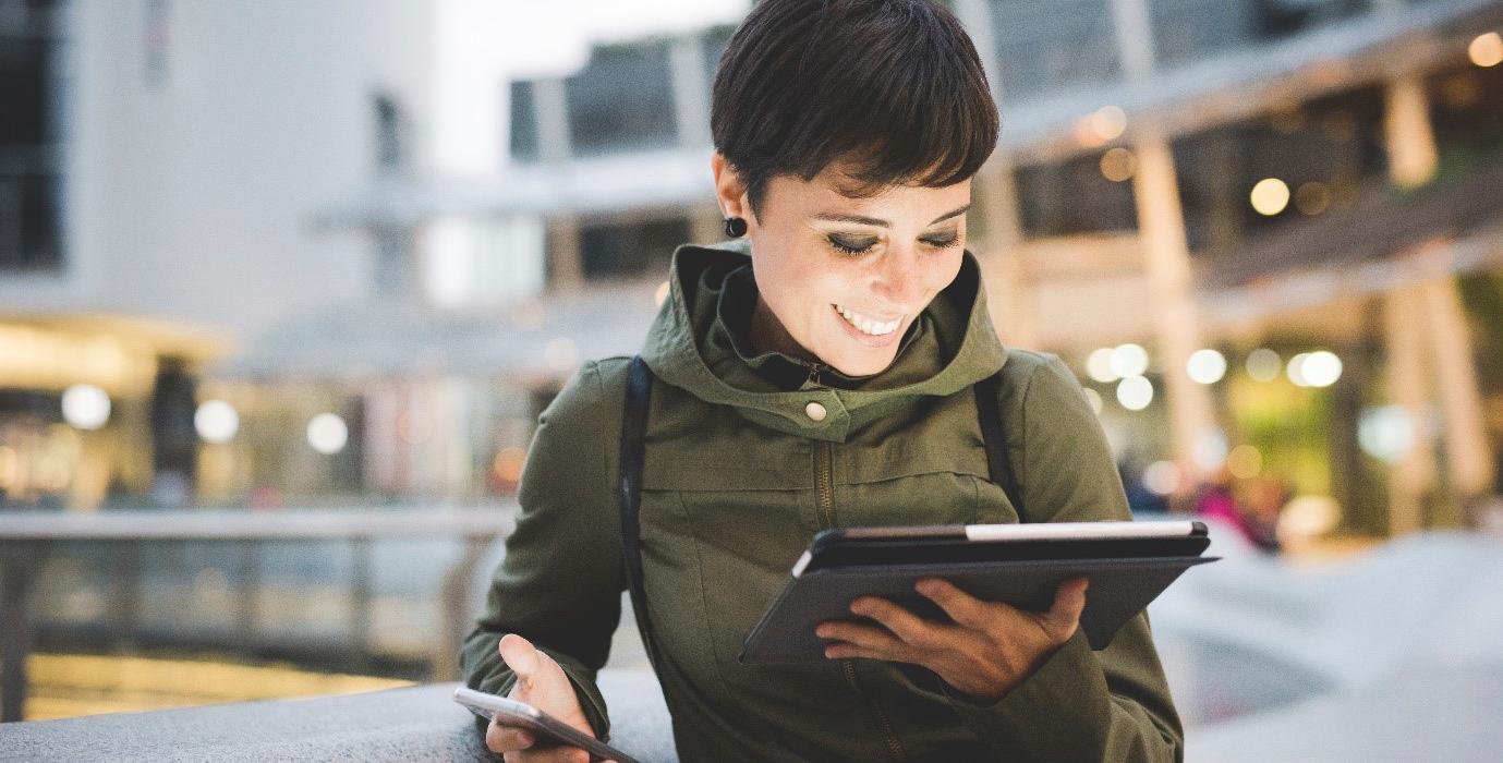 Woman smiles at her iPad while holding phone in other hand.