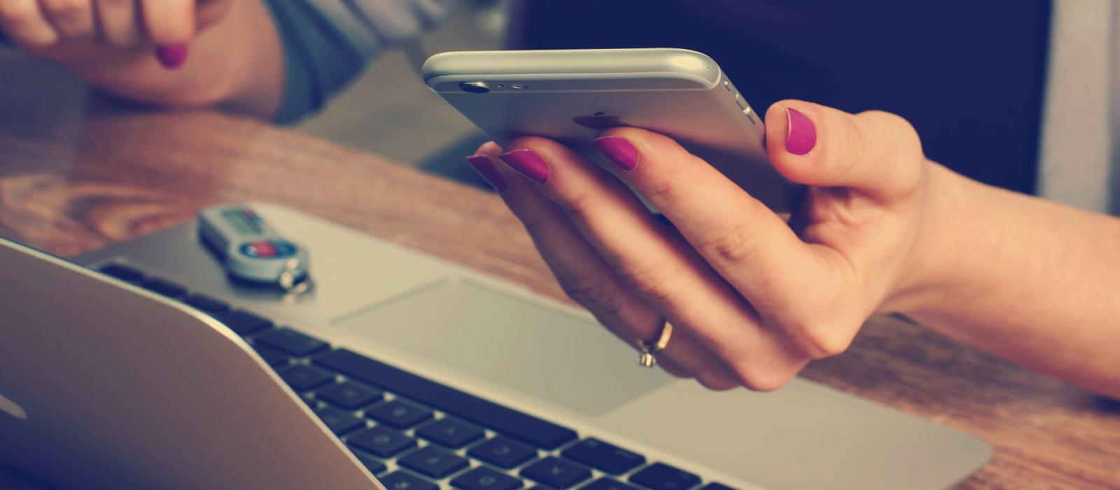 Woman hold iPhone as she works on Macbook