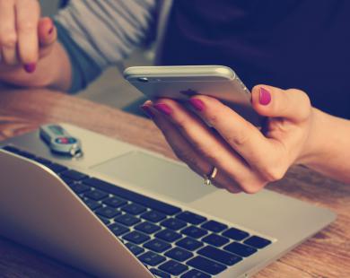 Woman hold iPhone as she works on Macbook